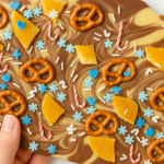 Chocolate Christmas bark with swirled dark and white chocolate, topped with pretzels, fruit pieces, and festive blue and candy cane sprinkles.