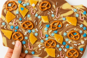 Chocolate Christmas bark with swirled dark and white chocolate, topped with pretzels, fruit pieces, and festive blue and candy cane sprinkles.